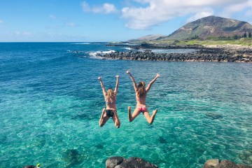 Two girls jumping off a cliff into the ocean in Hawaii